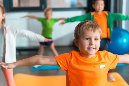 Selective focus of multiethnic kids doing exercise with outstretched hands in sports centerの写真素材