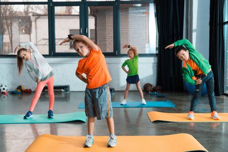 Selective focus of multicultural children warming up together on fitness mats in gymの写真素材