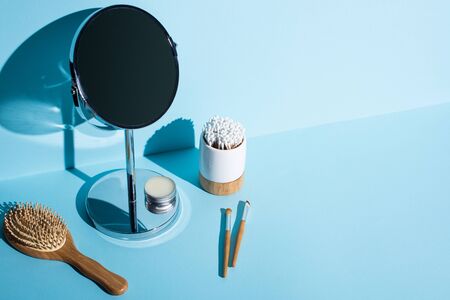 Mirror with jar of wax next to hair brush, cosmetic brushes, toothbrush holder with ear sticks on...