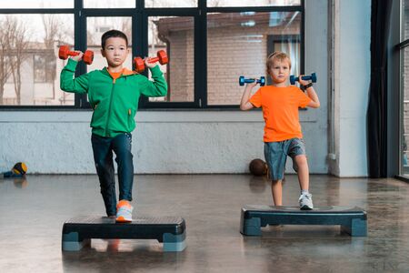 Front view of multicultural children holding dumbbells and doing Step Aerobics in gymの写真素材