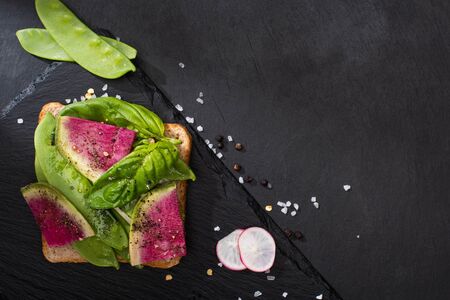 top view of organic radish sandwich on stone cutting board with pepper seeds and salt