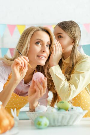 selective focus of kid whispering in ear of mother near easter eggs