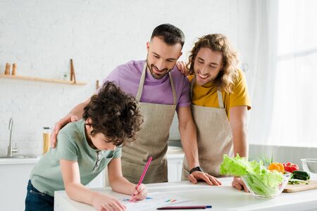 happy homosexual parents looking at mixed race kid drawing pictureの写真素材