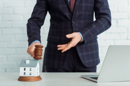 cropped view of auctioneer holding gavel and pointing with hand at model of houseの写真素材