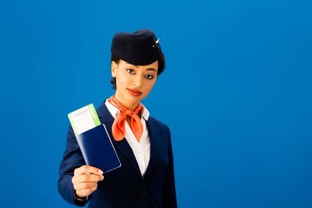 african american flight attendant holding passport and air ticket isolated on blueの写真素材