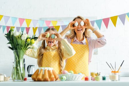 cheerful daughter and mother covering eyes with painted easter eggsの写真素材