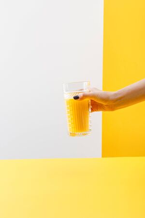 cropped view of woman holding glass of fresh delicious yellow smoothie on grey and yellow backgroundの写真素材