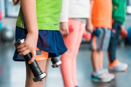 Cropped view of kids holding dumbbells in sports center