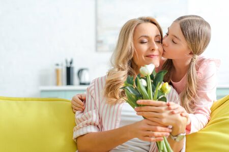 cute daughter kissing happy mother holding bouquet of tulipsの写真素材