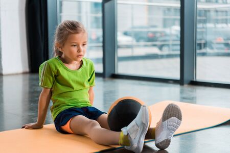Child with ball on legs sitting on fitness mat in gymの写真素材