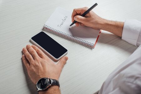 cropped view of translator writing in notepad with smartphone with blank screenの写真素材