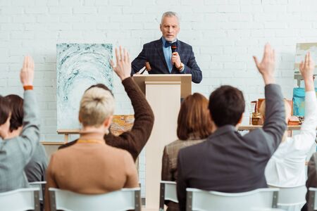 selective focus of auctioneer holding gavel and microphone and looking at buyers with raised hands during auctionの写真素材