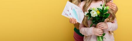 panoramic shot of mother and daughter holding tulips and greeting card with 8 march lettering isolated on yellowの写真素材