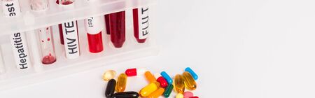 panoramic shot of test tubes with blood samples and lettering near pills isolated on white