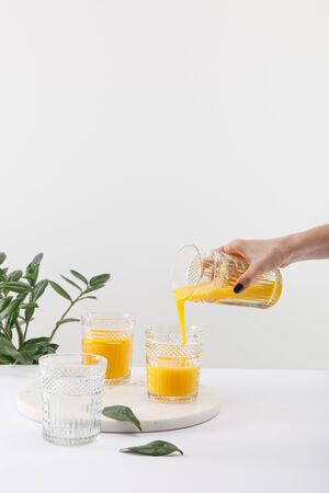 cropped view of woman pouring delicious yellow smoothie in glass near green plant isolated on whiteの写真素材