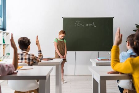 selective focus of schoolkid standing near chalkboard with class work lettering and classmates with raised handsの写真素材