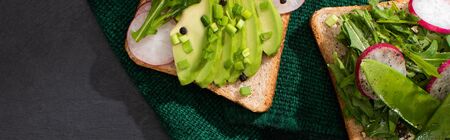 panoramic shot of vegetarian sandwiches with fresh radish and avocado on green cloth