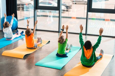 Back view of children with hands in air working out on fitness mats in gymの写真素材