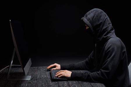hacker in hood looking at computer monitor with blank screen on black
