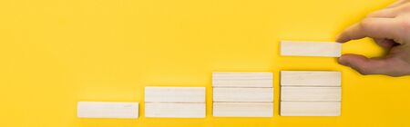 panoramic shot of man holding wooden block isolated on yellowの写真素材