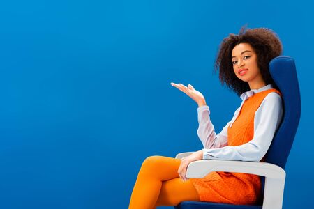 smiling african american in retro dress pointing with hand isolated on blueの写真素材