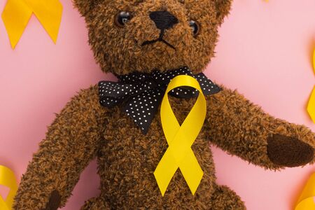 Top view of yellow ribbons with teddy bear on pink background, international childhood cancer day...