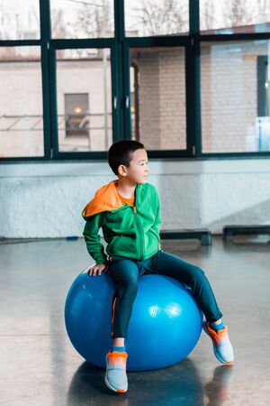 Selective focus of asian boy sitting on fitness ball in gymの写真素材