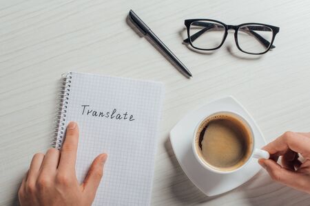 cropped view of translator with notepad, pen, eyeglasses and cup of coffeeの写真素材