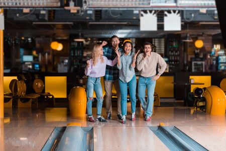 four cheerful multicultural friends standing near skittle alley in bowling clubの写真素材