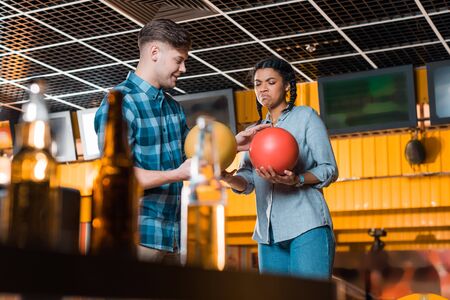 selective focus of smiling man talking to displeased african american girl while holding bowling ballsの写真素材