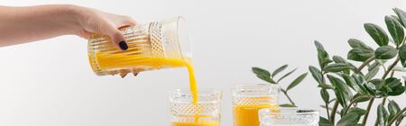 cropped view of woman pouring delicious yellow smoothie in glass near green plant isolated on white,...