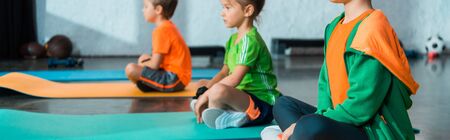 Selective focus of children with crossed legs sitting on fitness mats in gym, panoramic shotの写真素材