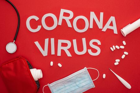Top view of pills, medical mask with stethoscope and coronavirus lettering on red background