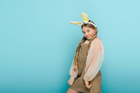 cheerful kid with bunny ears smiling isolated on blue