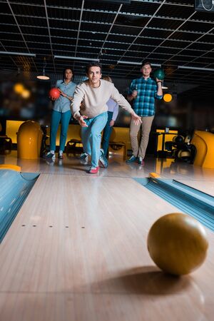 handsome young man throwing bowling ball on skittle alley near multicultural friendsの写真素材