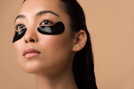beautiful asian girl with black hydrogel eye patches under eyes isolated on beige