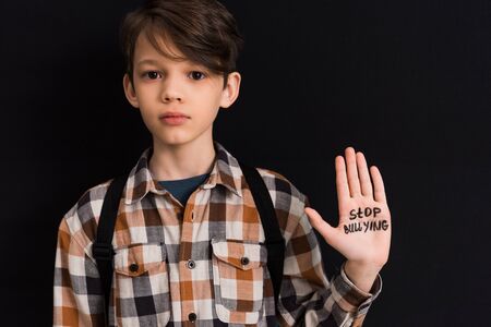 sad schoolboy with stop bullying lettering on hand isolated on blackの写真素材