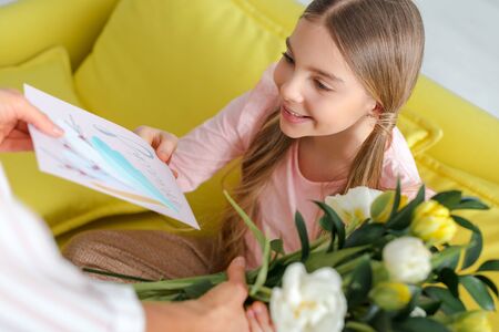 selective focus of happy child taking tulips and greeting card with 8 march lettering near motherの写真素材