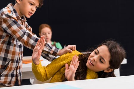 selective focus of cruel schoolboy bullying frightened schoolgirl near classmate