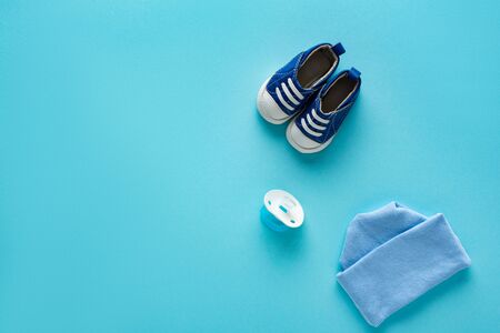 Top view of baby booties with hat and nipple on blue background, concept of mothers dayの写真素材
