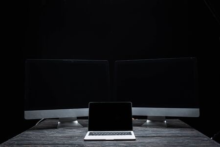 laptop with blank screen near computer monitors isolated on blackの写真素材