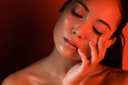 beautiful asian girl with silver sparkles on face and closed eyes in red lighting