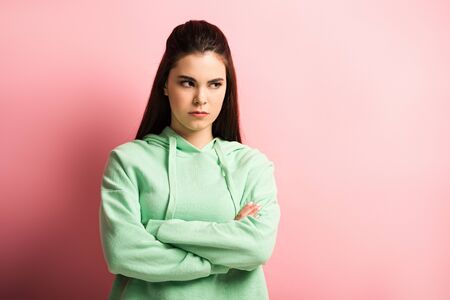 offended girl looking away while standing with crossed arms on pink background