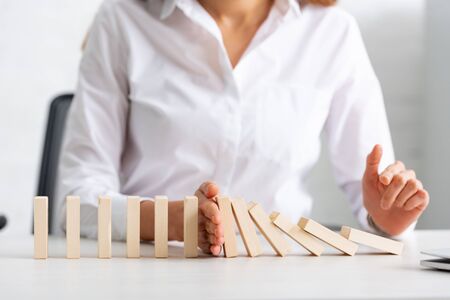 Selective focus of businesswoman holding falling building blocks on table