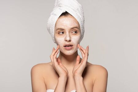attractive pensive girl with cosmetic mask on face and towel on head, isolated on grey