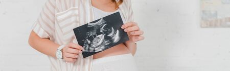 Cropped view of pregnant girl showing ultrasound scan of baby, panoramic shot