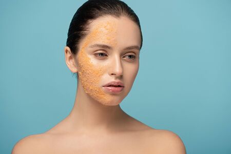 attractive girl applying yellow sugar exfoliant on face, isolated on blueの写真素材