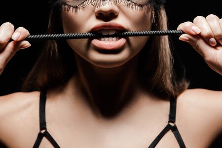 cropped view of seductive woman holding flogging whip in mouth isolated on blackの写真素材