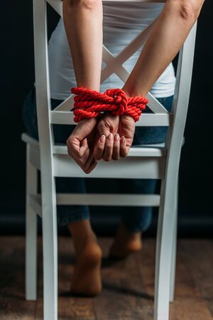Cropped view of woman with tied hands on chair on black backgroundの写真素材