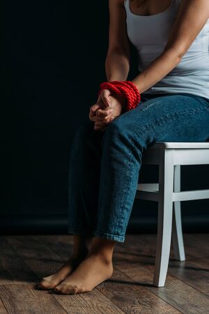 Cropped view of woman with tied hands sitting on chair on black backgroundの写真素材